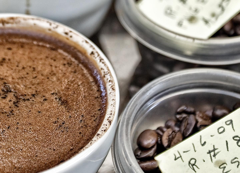 Coffee beans are in different containers next to a cup of Coffee.